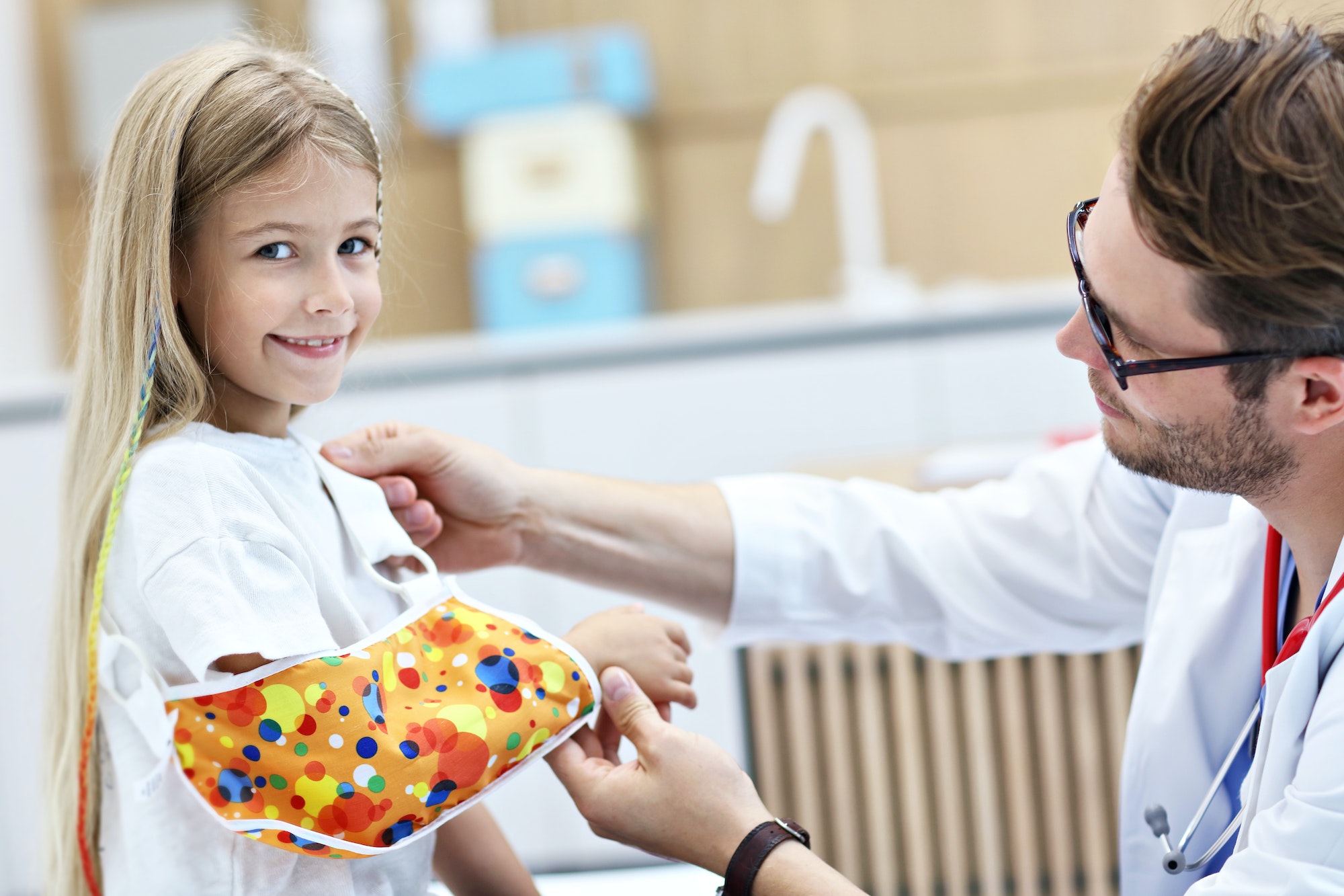 Male pediatrician checking bandage of little girl's broken arm