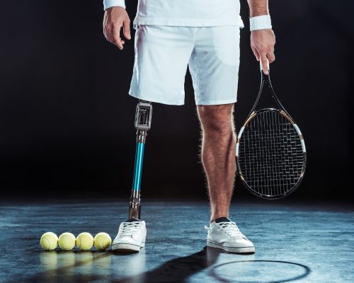 cropped shot of paralympic tennis player with racket in hand and tennis balls on floor