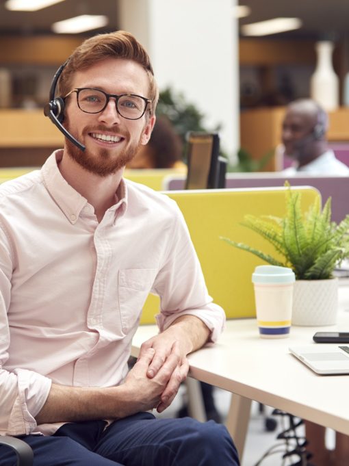 Portrait Of Businessman Wearing Headset Talking To Caller In Customer Services Centre